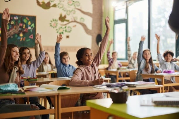Stock photo of happy elementary students raising their hands in class
